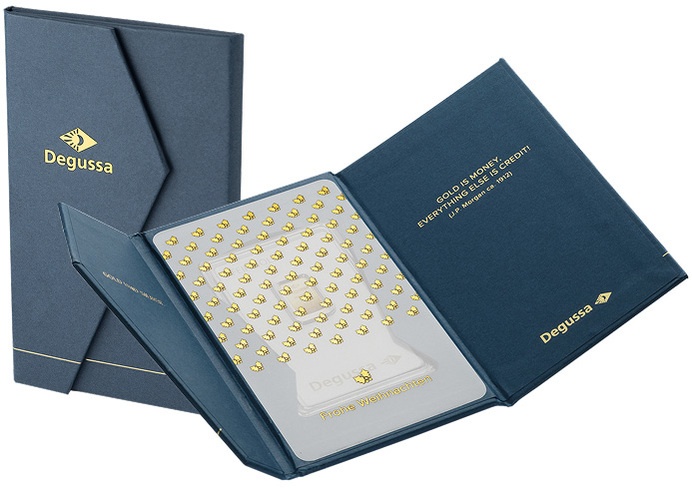 Aufgeklapptes dunkelblaues Degussa-Geschenketui mit Goldbarren und Anlasskarte, daneben die geschlossene Hülle mit goldenem Degussa-Logo.